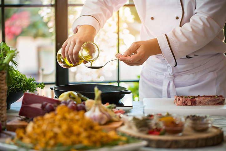 Kochen mit Fett Ein Koch portioniert Öl zum Braten in der Pfanne mit einem Esslöffel.